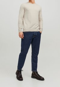 Beige stickad tröja med långa ärmar och ribbade muddar, kombinerad med mörkblå denimjeans och svarta snörkängor.