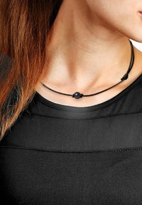 Collier en cordon noir avec une perle centrale foncée, design minimaliste, longueur ajustable et texture lisse. Porté au-dessus d'un vêtement noir.