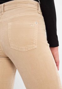 Beige corduroy broek met een achterzak met een metalen accent. De gestructureerde ribbel geeft visuele interesse aan de stof.