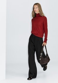 Rood coltrui, zwarte wijde broek en een bruine suède schoudertas met zilveren hardware. Zwarte platte sandalen maken de look af.