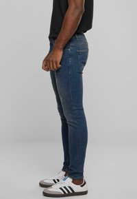 Jeans ajustados de mezclilla azul con una textura ligeramente desgastada, combinados con zapatillas blancas y grises que tienen rayas negras.