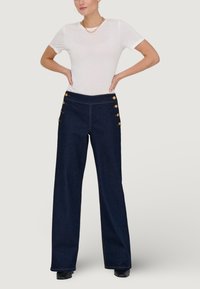Mariene wijde jeans met gouden knoopaccenten bij de taille, gecombineerd met een aansluitend wit T-shirt. Gladde denimtextuur; rechte zoom.