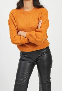 Orange knitted sweater with a round neckline and long sleeves, paired with black leather pants, showcasing a smooth texture and fitted design.