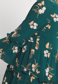 Teal blommig klänning med fjärilstryck, med volangärmar, ett lager-på-lager-design och en lätt tygtextur.