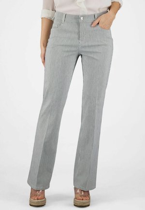 Vrouw draagt grijs-witte fijn gestreepte hoge taille broek met rechte pijpen en zakken, gecombineerd met een witte blouse en platformsandalen.