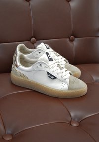 Sneaker bianche in pelle con punta in suede e dettagli dorati, dotate di una suola in gomma testurizzata e un patch logo nero di lato.