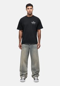 Czarna bawełniana koszulka o luźnym kroju, z białym napisem z przodu. Para wyblakłych jasnoniebieskich dżinsów, noszonych z czarno-białymi trampkami.