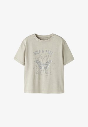 Camiseta de manga corta color beige claro con mariposa plateada, llamas y las frases "WILD & FREE" y "BORN TO FLY" impresas en la parte delantera.