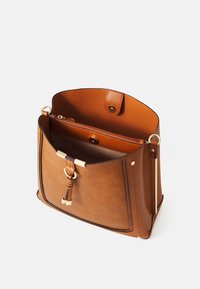 Brun læderhåndtaske med en glat tekstur, magnetlukning og hardware i guldtoner. Indvendigt har den et rum med lynlås og detaljer.