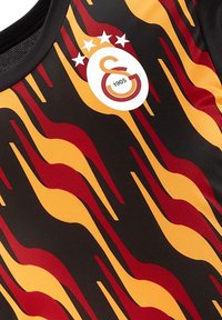 Zwart shirt met een golvend patroon in rood en geel. Centraal logo met drie sterren erboven en het jaar "1905" eronder. Gladde textuur.