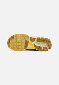 Sola de sapato com uma textura em relevo e padrão em borracha. As cores incluem bege, branco e acentos vibrantes em amarelo. Apresenta ranhuras profundas para tração.