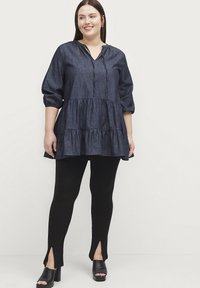 Denim tunika med lagdelt design, knaplukning og 3/4 ærmer, parret med sorte leggings med sideslids og blokhæle.