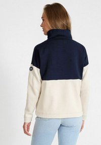 Mörkblå och krämfärgad färgblockad sweatshirt med hög krage och cirkulärt logo på vänster ärm. Mjuk fleece-textur och avslappnad passform.