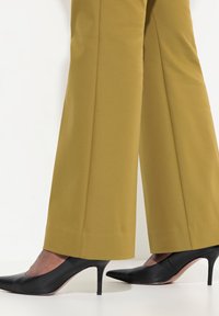 Svarta högklackade skor med spetsig tå och slät yta, bärs med skräddarsydda byxor i senapsgul färg med en ren, rak ben-design.