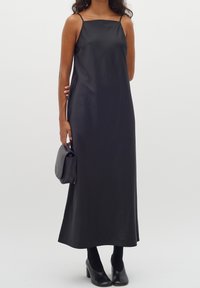 Czarna, bezrękawnikowa sukienka maxi wykonana z gładkiego materiału, z cienkimi ramiączkami i prostym krojem. W zestawie z czarnymi szpilkami i kopertówką.