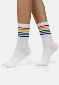 Witte enkel sokken met horizontale regenboogstreepjes in rood, oranje, geel, groen, blauw en paars aan de geribbelde bovenrand. Zachte textuur.