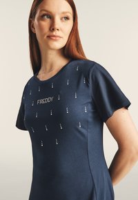 Camisa de manga corta azul marino hecha de una tela suave, con un patrón de puntos con pequeños rhinestones y el nombre de la marca "FREDDY" en cristales.