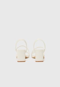 Sandales blanches à talons avec des fines lanières, design à talon bloc, texture lisse et style minimaliste. Le talon mesure environ 5 cm.