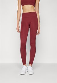 Colanți mulați burgundy cu talie înaltă, fabricați din material elastic. Asociați cu pantofi sport albi pentru un aspect sportiv.