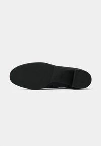Sola de sapato preta com uma superfície texturizada e um ligeiro salto. O material parece borrachoso, com um acabamento suave e um design minimalista.