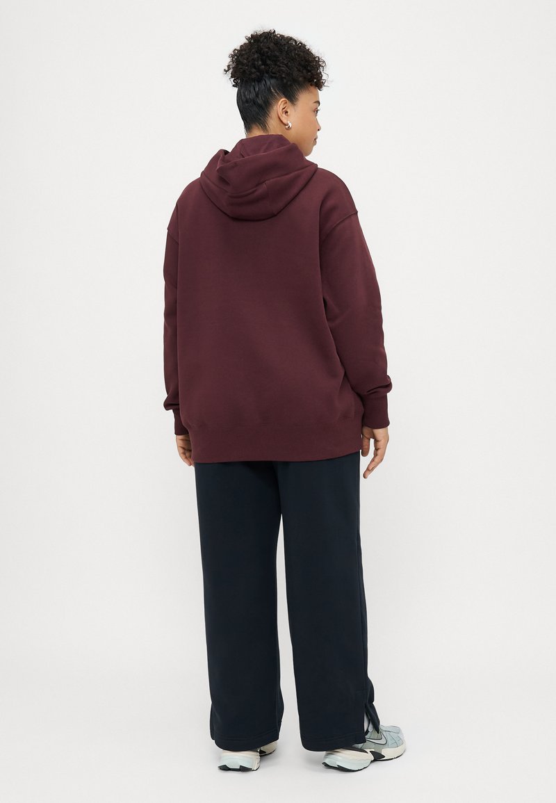 Übergroßer burgunderfarbener Hoodie mit Kapuze, kombiniert mit lockeren schwarzen Hosen. Das Outfit hat eine bequeme Textur und eine lässige Passform, ideal für Alltagskleidung.