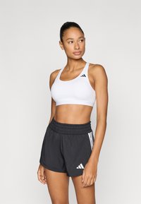 Άσπρο αθλητικό σουτιέν με μαύρες λεπτομέρειες, σε συνδυασμό με μαύρο σορτς που διαθέτει ελαστική μέση και λευκές ρίγες στα πλαϊνά.