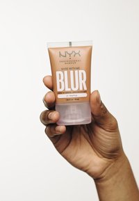 Fond de teint NYX Bare With Me Blur, 30 ml, en teinte Truffle. Design de tube compressible avec une base translucide, un bouchon de couleur bronze et un texte blanc audacieux.
