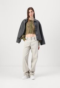 Manteau court gris sur un haut brodé vert, assorti à un jean large de couleur claire et des baskets blanches. Design simple et moderne.