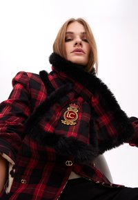 Rød- og sort rutet frakke med sort faux fur-krave og guld LC-emblem. Udstyret med guldfarvet metaldele og en skræddersyet pasform.