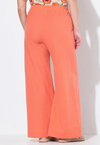 Wijdvallende broek in koraaloranje stof met een elastische tailleband. Zachte textuur, volledige lengte en een relaxte pasvorm.