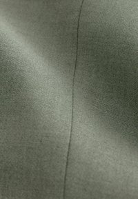 Tissu vert olive lisse avec une couture subtile verticale, montrant un tissage finement texturé et de légers plis.