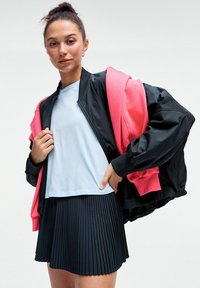Črna bomber jakna z roza akcenti, svetlo modra majica in črna plisirana krila. Ima zadrgo spredaj in rebraste manšete.