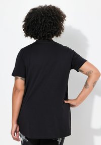 Sort T-shirt med korte ærmer og rund halsudskæring, som har en længere bagkant og en glat bomuldsstruktur.