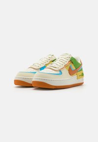Witte leren sneakers met kleurrijke accenten in groen, blauw, oranje en geel. Textuur van oranje rubberen zool en geperforeerde neus.