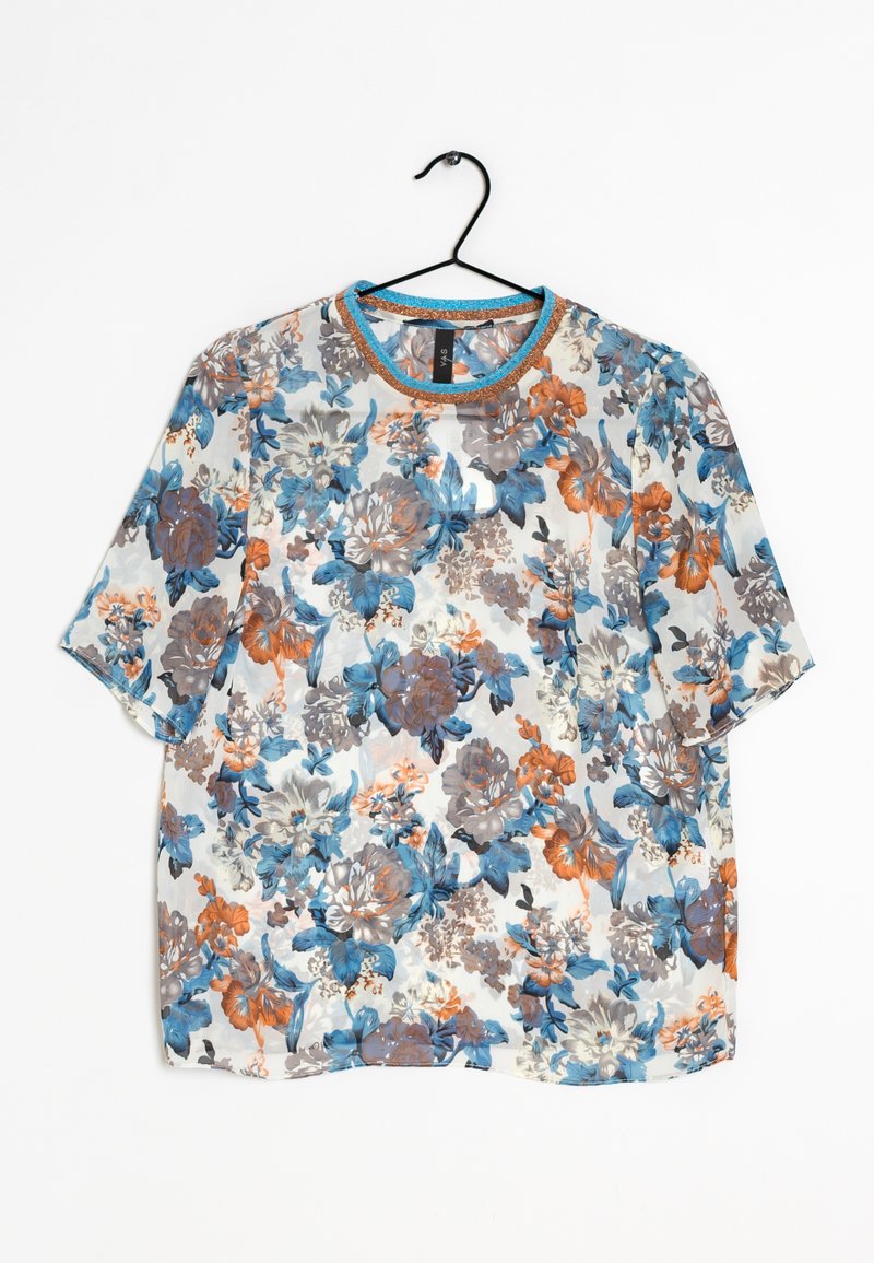 Blouse à manches courtes à fleurs bleues, orange et grises sur tissu blanc, suspendue sur un cintre noir.