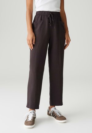 Donkerbruine, losse broek met een verstelbare taille, zijzakken en een gladde textuur, gecombineerd met bruin en witte sneakers.