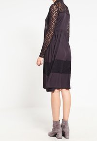 Vestido de manga larga con un cuerpo de encaje, mitad inferior negra sólida y corte a la altura de la rodilla. Combinado con botines de ante grises.