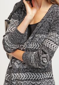 Stickad cardigan med ett svartvitt mönster, med långa ärmar, en djup V-urringning och texturerade detaljer längs fållen och manschetterna.