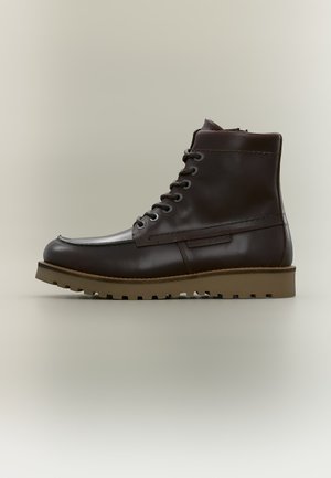 Dunkelbrauner Leder-Schnür-Stiefeletten mit einer tanfarbenen Gummiprofilsohle, glatter Oberfläche und seitlichen Ziernähten, seitlich vor neutralem Hintergrund dargestellt.