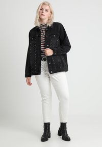 Sort denimjakke med sølvnitter, lange ærmer, forlommer, parret med en stribet turtleneck og hvide jeans, afsluttet med sorte ankelstøvler.