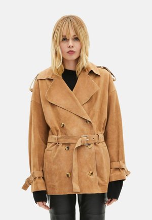 Brun ruskind dobbeltbrystet trenchcoat med bælte i taljen, store knapper og opviklede ærmekanter. Har brede revers og en afslappet pasform.