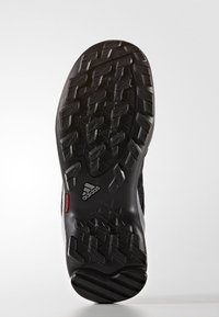 Czarna gumowa podeszwa buta Adidas z teksturowanym wzorem bieżnika i małym czerwonym akcentem na czystym białym tle.