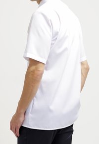 Camicia a maniche corte con colletto in tessuto bianco, caratterizzata da una texture liscia e una vestibilità comoda, senza motivi o accenti visibili.
