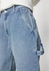 Light blue denim cargo pants with a relaxed fit, featuring side pockets and decorative loops for additional detailing.