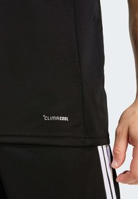 Μαύρο αθλητικό πουκάμισο με ομαλή υφή, με λογότυπο "CLIMACOOL" και λευκές οριζόντιες ρίγες στο πλάι.