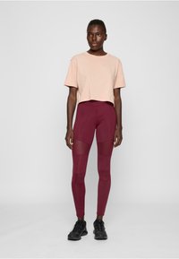 Lys rosa cropped t-skjorte kombinert med burgunder leggings som har mesh-paneler og en glatt tekstur; svarte treningssko fullfører antrekket.