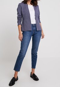Námořnický texturovaný blazer, bílý tričko a tmavě modré džíny. Černé loafery. Blazer má elegantní design s šálovým límcem a bez knoflíků.