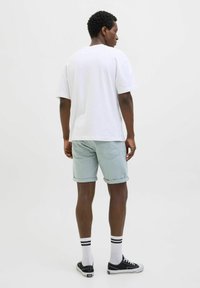 Vit bomull t-shirt, ljusgröna shorts med uppvikta fållar, svarta sneakers och vita strumpor med svarta ränder. Enkel design, avslappnad passform.