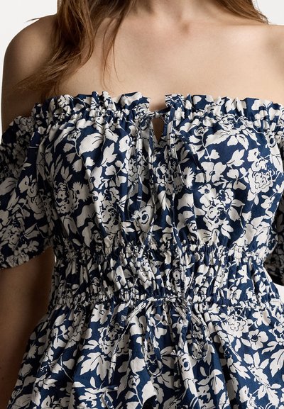 Zils un balts ziedu off-shoulder kleita ar elastīgu jostu, pūkainām piedurknēm, šūtu dekoru un atslēgas caurumu izgriezumā.