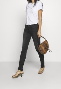 Jeans skinny negros, camiseta blanca, tacones dorados con tiras, y un bolso marrón con estampado de serpiente y una asa corta. Diseño minimalista, ajuste elegante.